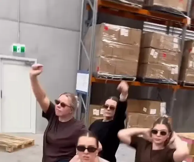 Fayt deposunda koliler önünde birlikte dans eden çalışanlar
